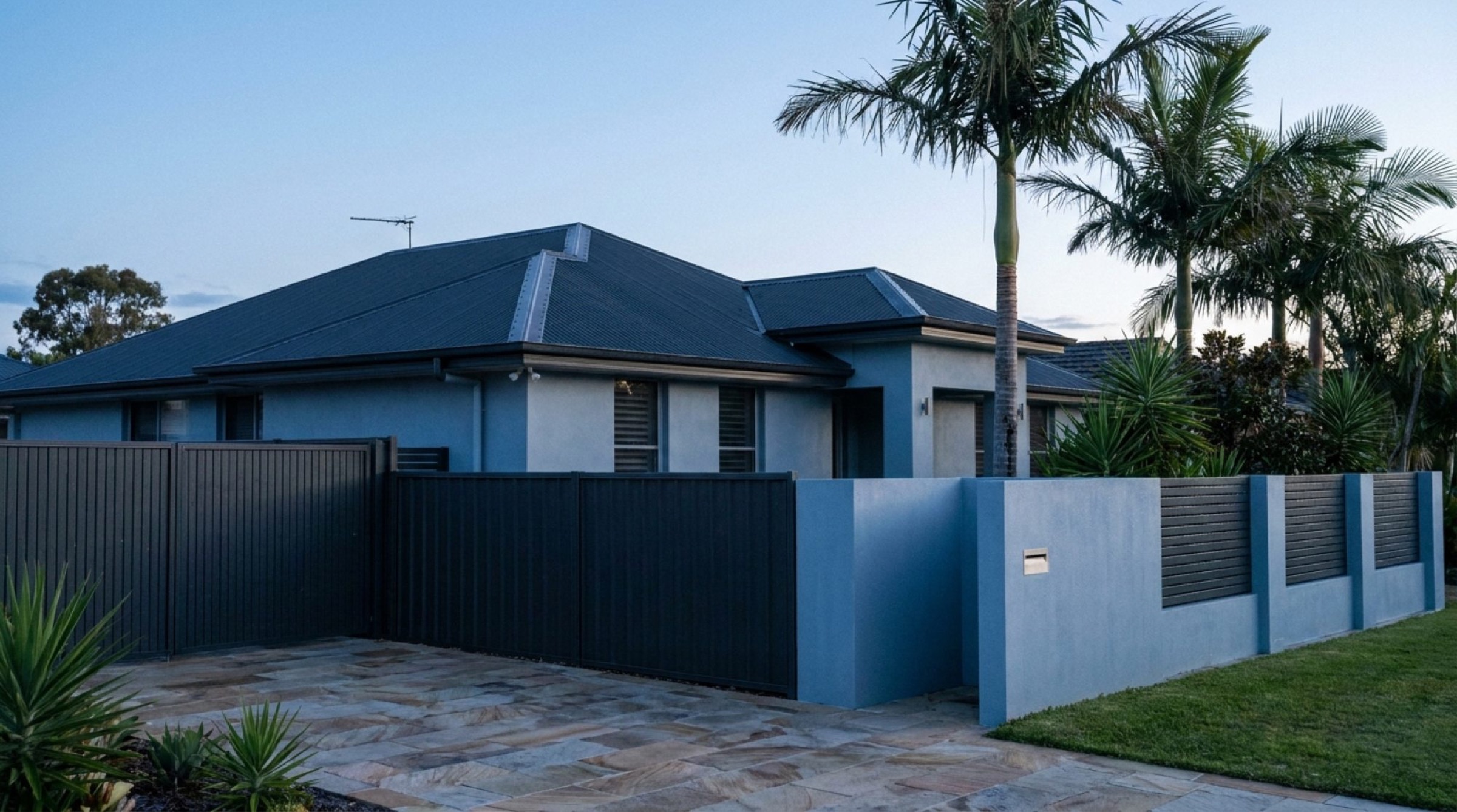 A rendered Queensland home with a metal roof and palms at dusk