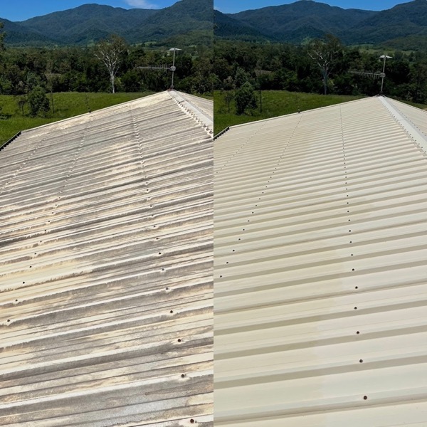 A corrugated metal roof with a clear line between the stained section and the washed section, hills behind