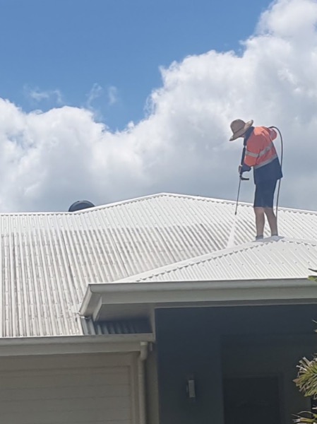 A worker in hi-vis washing a white metal roof under heavy cloud