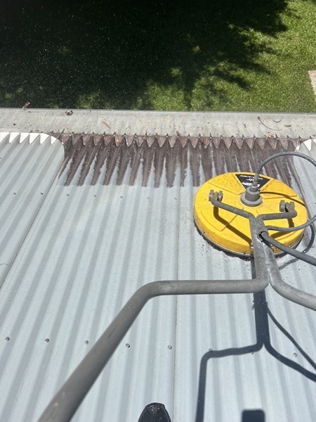 A yellow rotary surface cleaner resting on a corrugated metal roof