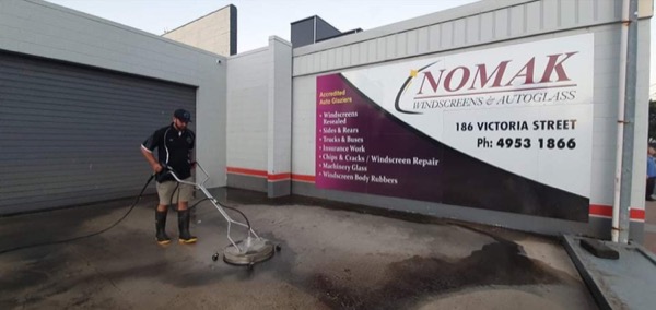 A worker running a surface cleaner across the concrete outside a commercial building