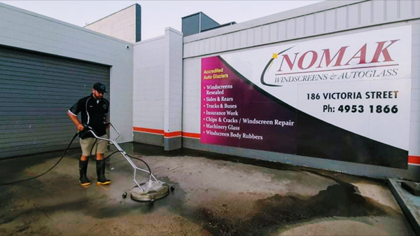 A worker cleaning concrete outside a commercial premises with a roller door behind