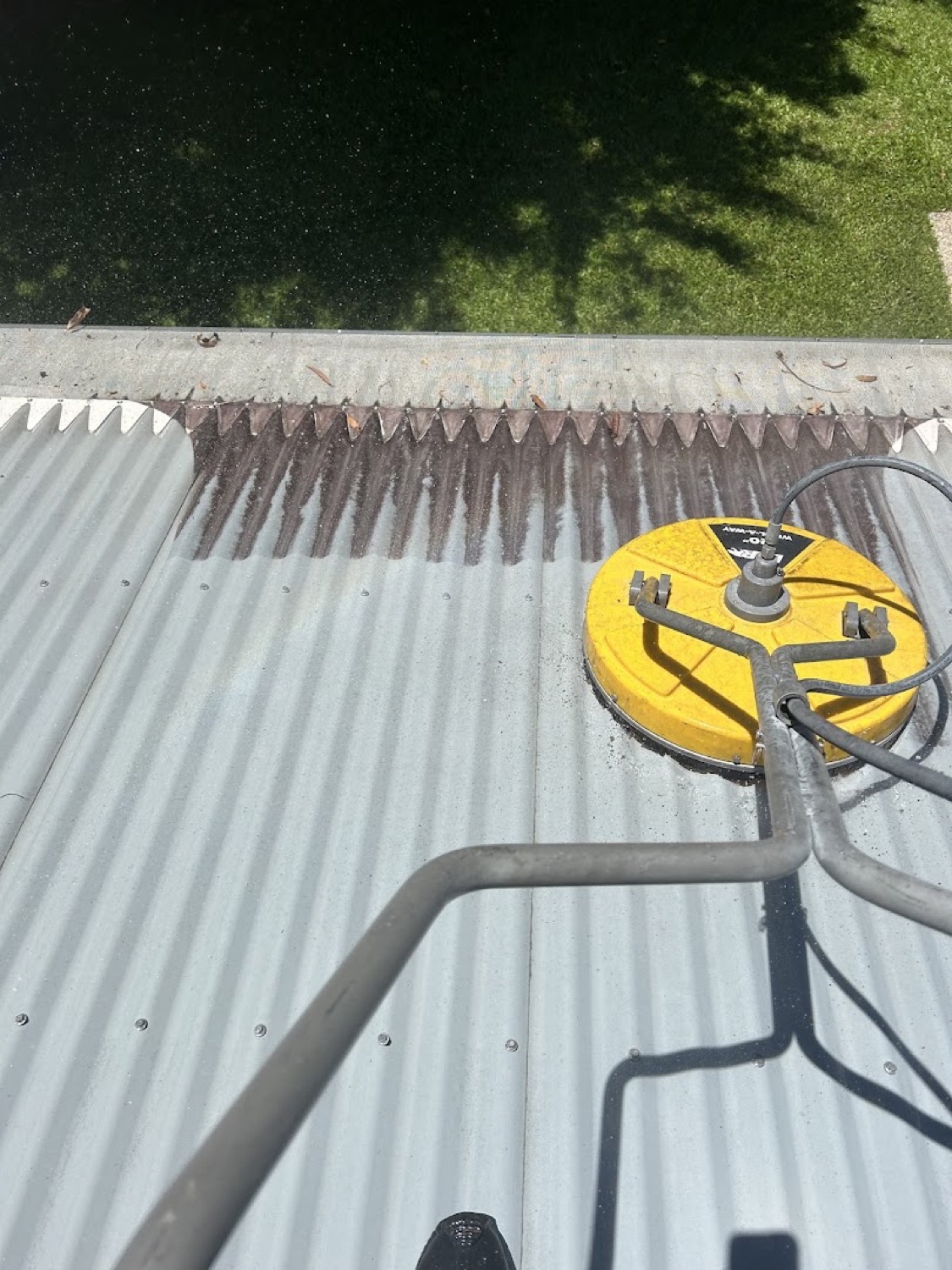 A rotary surface cleaner sitting on a corrugated metal roof