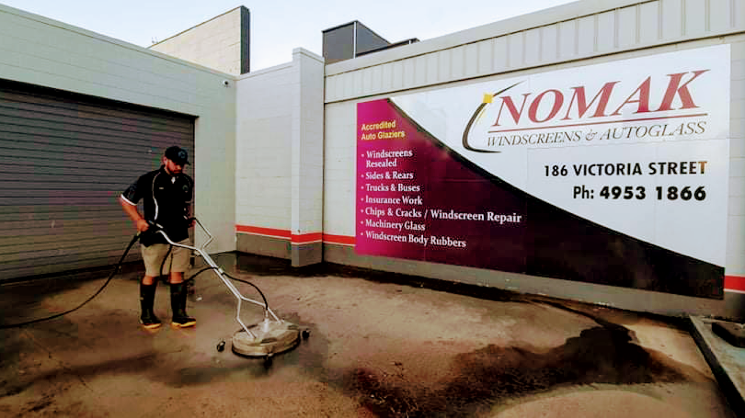 A worker cleaning the concrete apron in front of a roller door