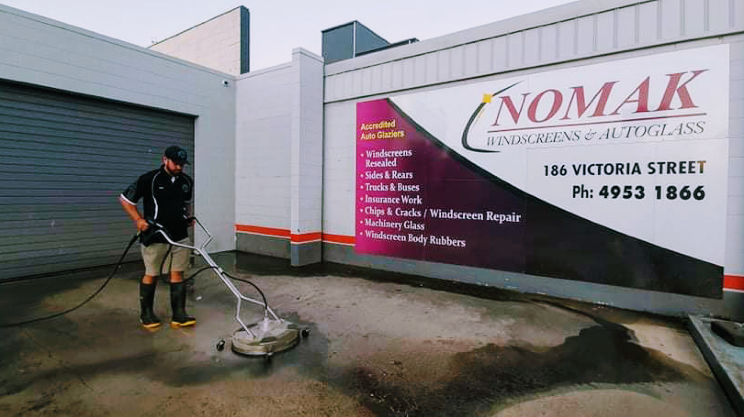 A worker cleaning a commercial forecourt with a surface cleaner beside a roller door